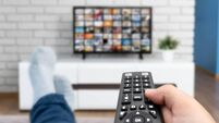 Man watching TV, lying on sofa, legs on table