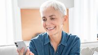 Happy mature woman in casual clothes using cellphone for online shopping from home.