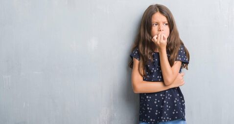 Young hispanic kid over grunge grey wall looking stressed and nervous with hands on mouth biting nails. Anxiety problem.