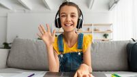 Girl in headphones using laptop, waving hand to webcam