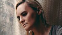 Blonde woman sitting by the rainy window, looking absently out, sad