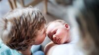 A small boy kissing a sleeping newborn baby brother at home.