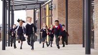 Primary school kids, wearing school uniforms and backpacks, running on a walkway outside their school building, front view