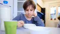 Boy sitting at the dining room table and eating breakfast in bowl