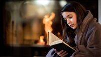 Young girl reading a book by the fireplace