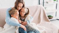 caring mother wrapping sick children in blanket while sitting on sofa