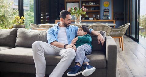 Dad talking with his smiling little son on a sofa at home
