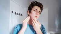 Concentrated caucasian teenage boy with acne problem at his face looking in mirror at home bathroom. Teenager skin care every da