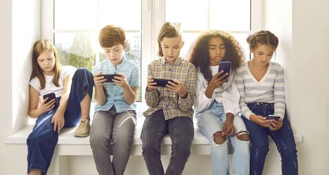 Children sitting on windowsill, playing online games on mobile phones and ignoring each other