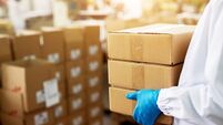 Close up view of a dedicated worker carrying a stack of duck taped brown boxes in factory storage room while wearing sterile clo
