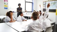 High School Students Wearing Uniform Raising Hands To Answer Question Set By Teacher In Classroom